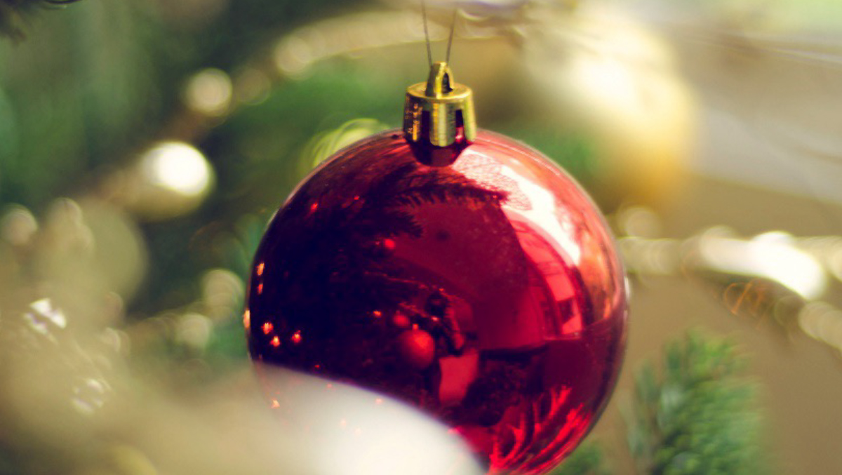 Photo of a close-up of a round red ornament hanging on a Christmas tree.