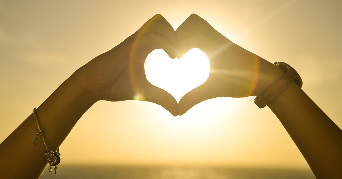 Two hands forming a heart with the sun shining through